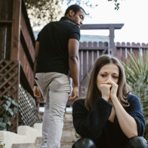 Woman sitting on steps looking worried with hand on her face, while man walks away up the steps and looks back at her