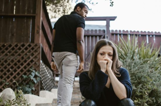 Woman sitting on steps looking worried with hand on her face, while man walks away up the steps and looks back at her